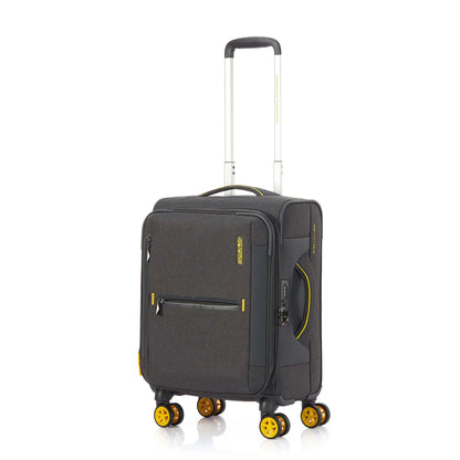 Angled view of the American Tourister Droyce soft-shell spinner in Grey, featuring a modern dip-dye color gradient, yellow accents, and a distinctive metal logo. Shop Now Online