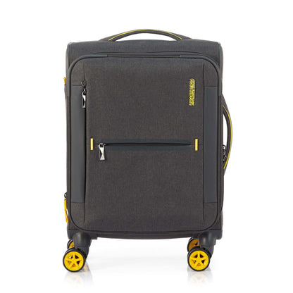 Front view of the American Tourister Droyce soft-shell spinner in Grey, featuring a modern dip-dye color gradient, yellow accents, and a distinctive metal logo. Shop Now Online