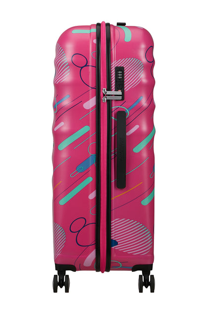 Side view of the American Tourister Disney Wavebreaker spinner in Pink, showing the zipper and a textured, wave-patterned hardshell. Find Now Online